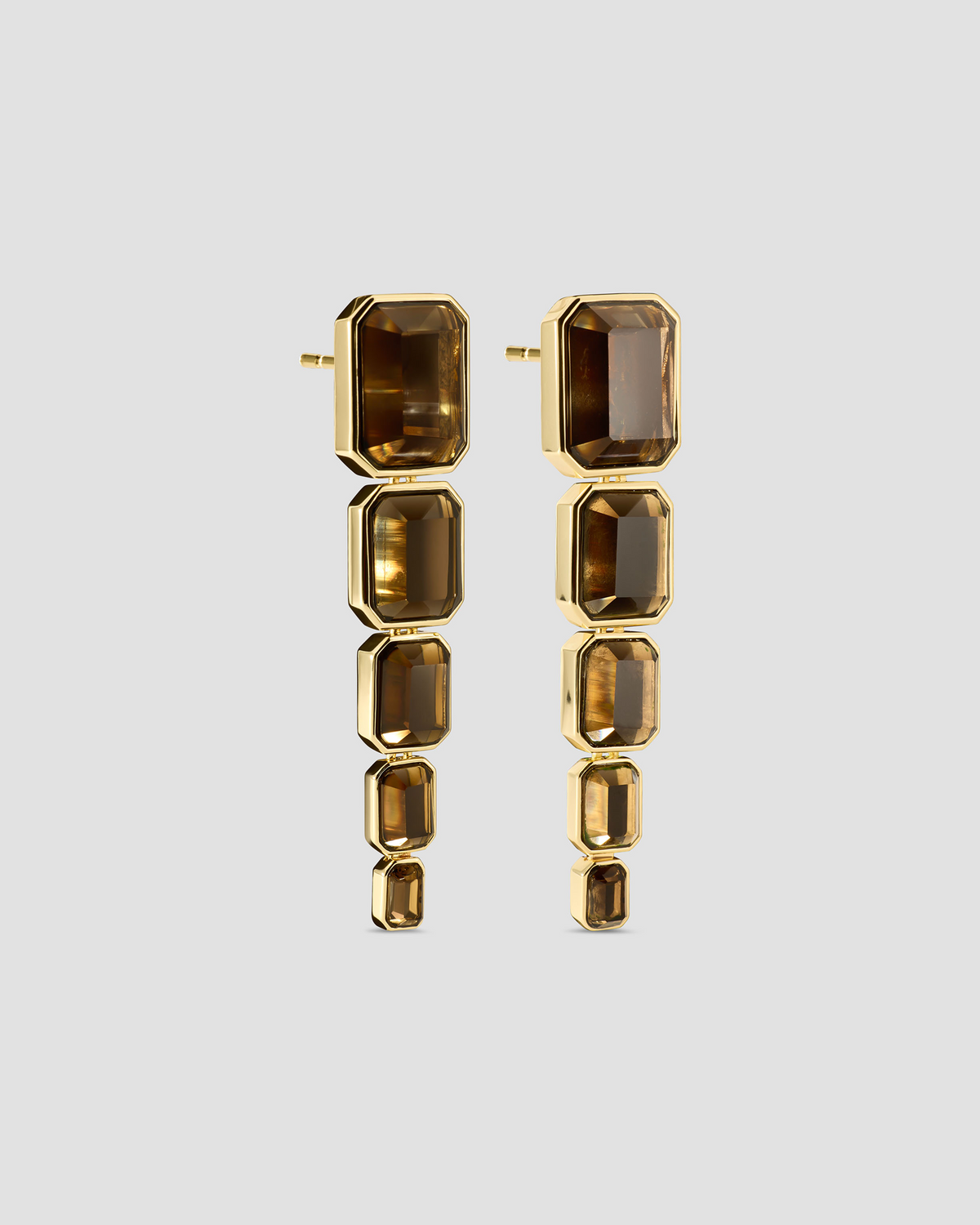 A pair of gold drop earrings featuring a series of stacked rectangular smoky brown gemstones, shown against a solid light gray background.