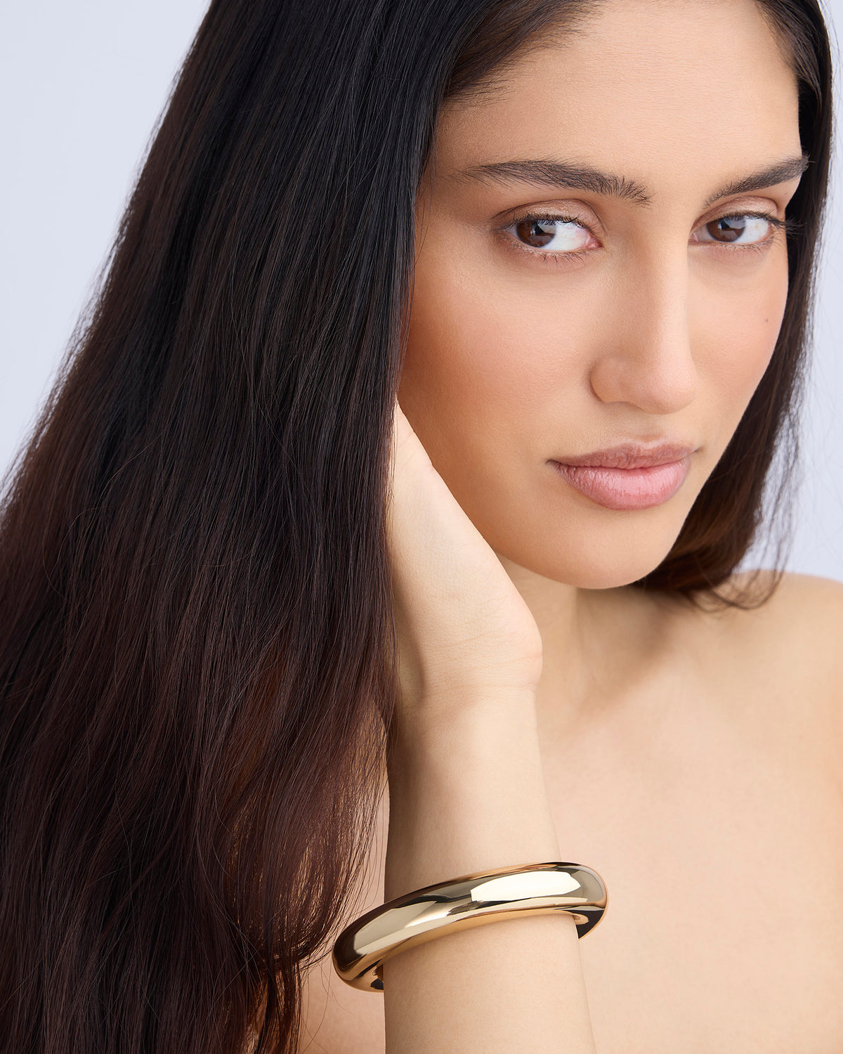 Woman wearing a gold bracelet on a plain background