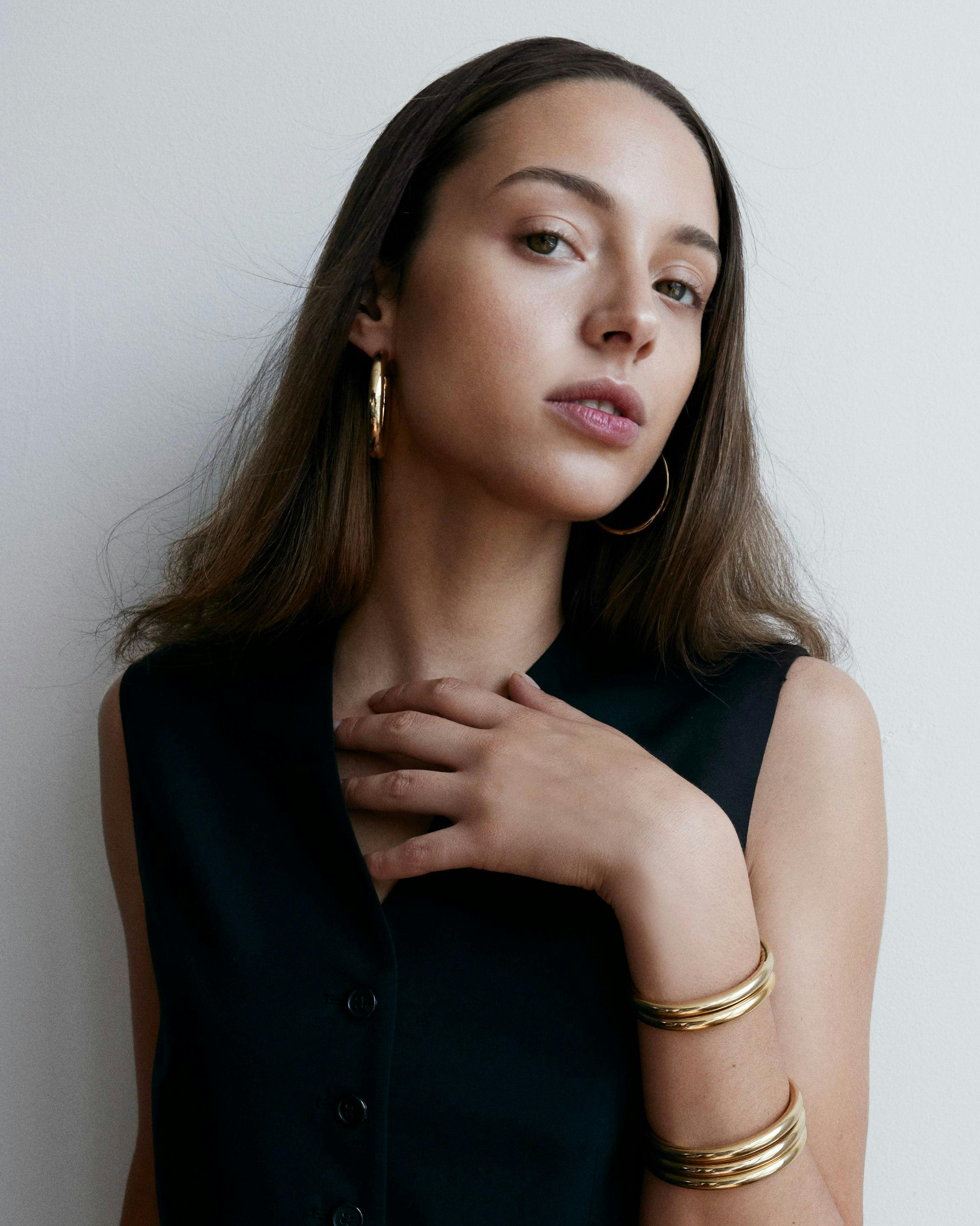 Model wearing gold hoops and multiple gold bangles 