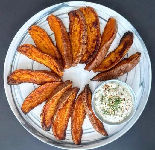 Plate of roasted sweet potato wedges with bowl of creamy dill dip. 
