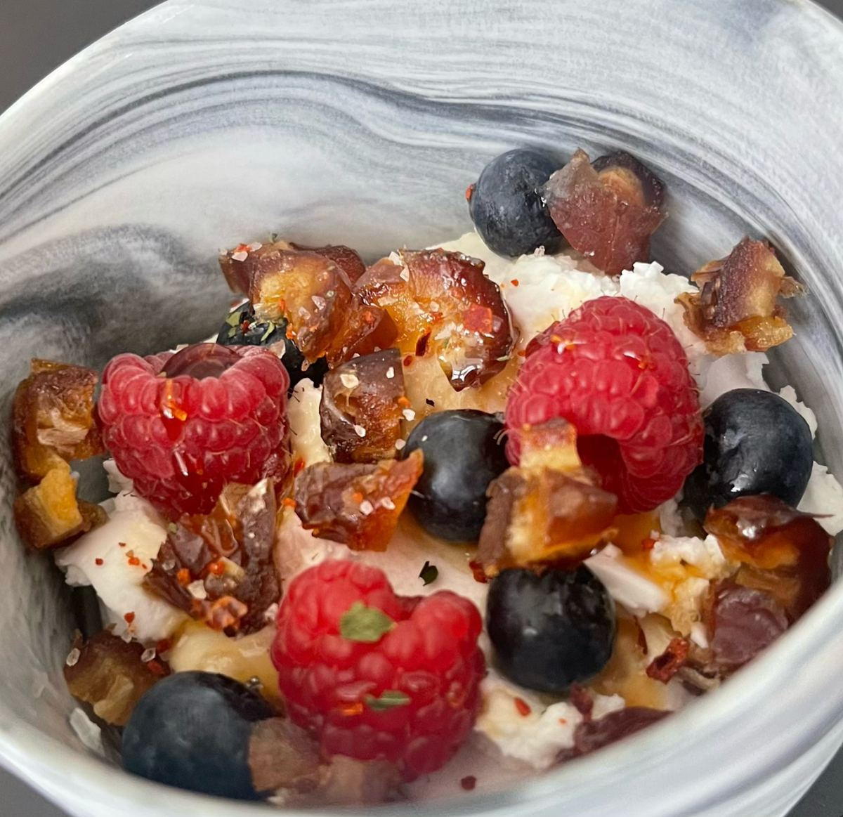 Close up picture of Sweet and spicy yogurt bowl in a bowl. Features berries, yogurt, dates, and more.