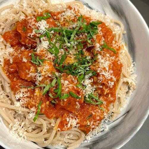 Bowl of warm spaghetti covered with JF Simple tomato sauce, chicken meatballs, and basil. 