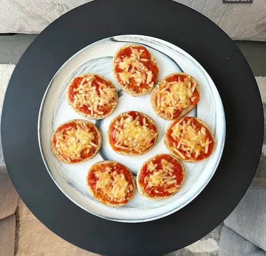 Plate of mini sized snack pizzas topped with tomato sauce and vegan mozzarella cheese.