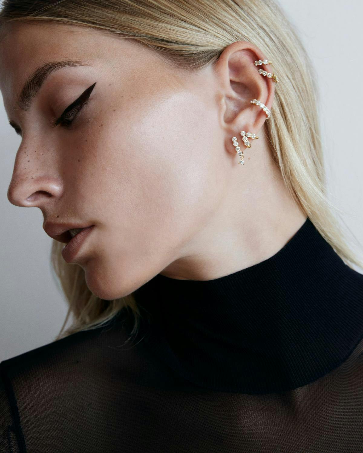 Model wearing multiple diamond huggie earings. 