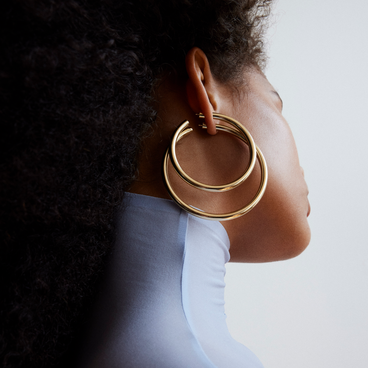 A close up shot of a model wearing two oversized hoop earrings facing away from the camera