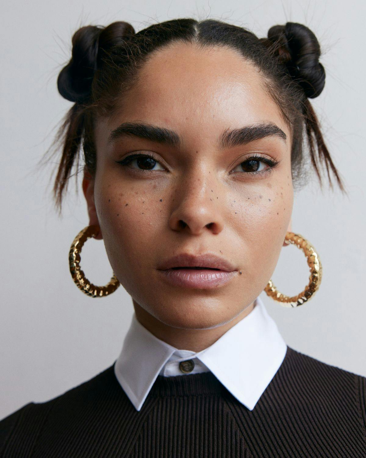 Woman looking directly into camera wearing nice clothes and a gold pair of hoops