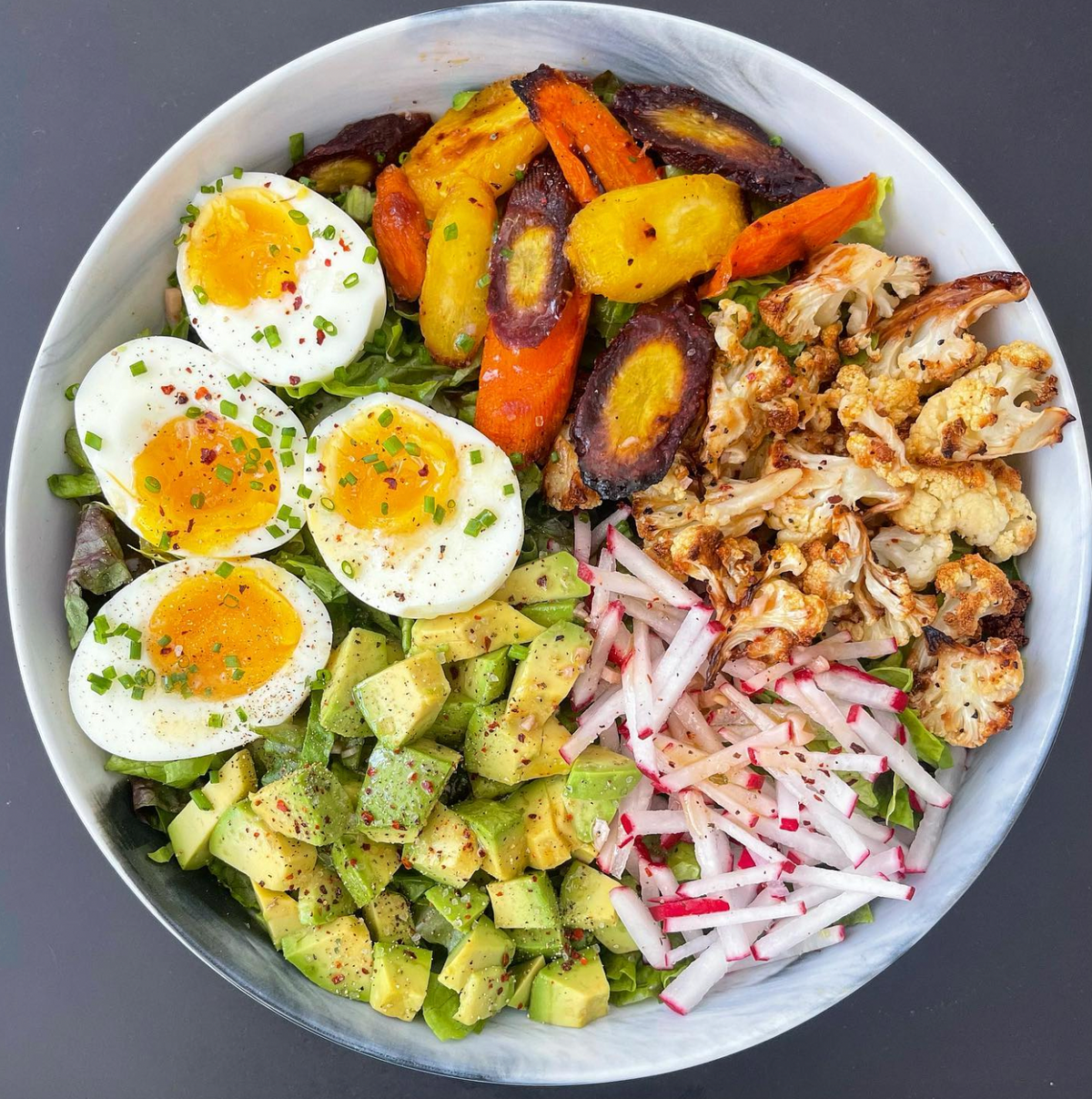Picture of bowl of salad with eggs, avocado, radish, cauliflower, and more.
