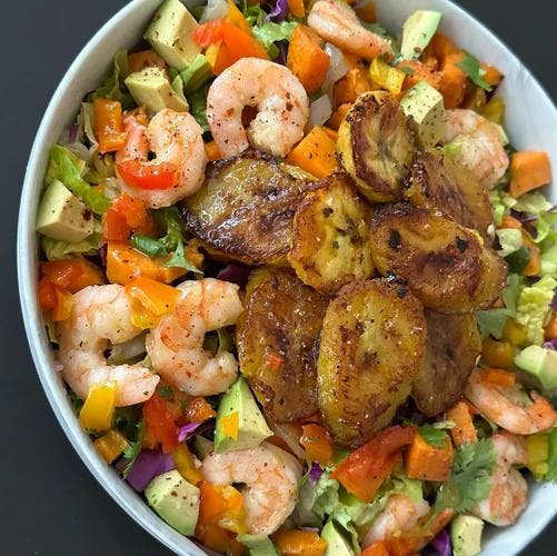 Salad bowl filled with greens, avocado, red, yellow, and orange peppers, shrimp and pan fried plantains. 