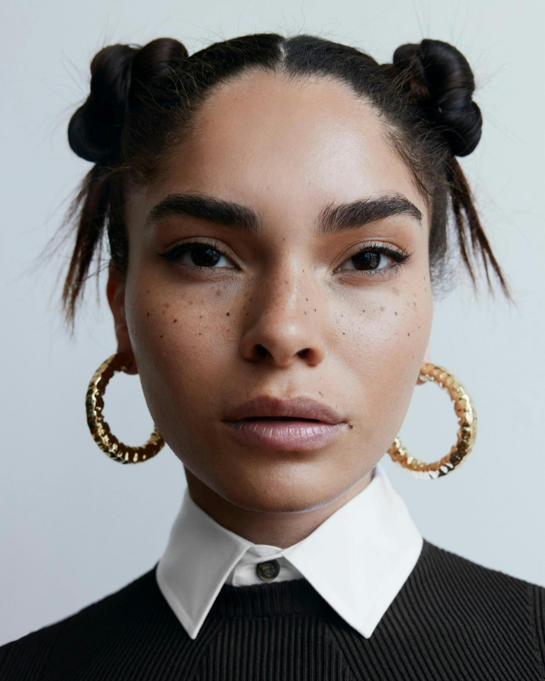 Model looking into camera wearing space buns and textured gold hoops