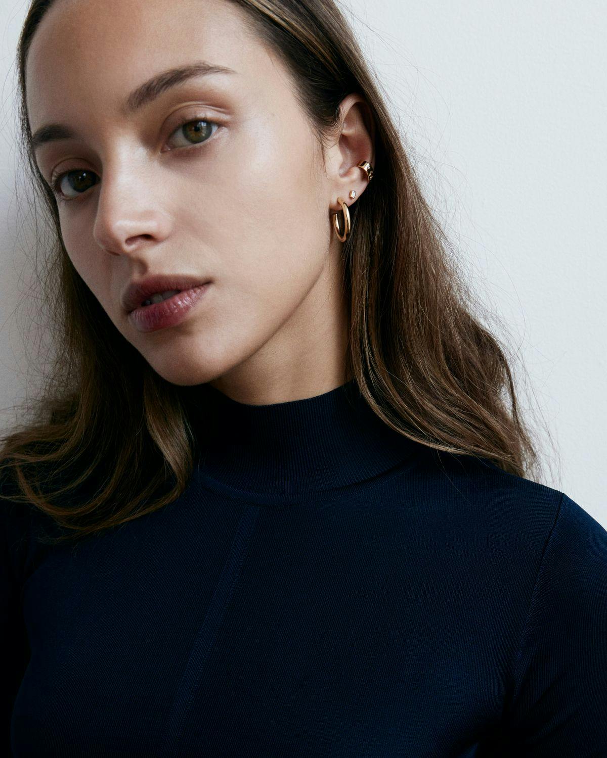 Model wearing high collar turtleneck and diamond earrings. 