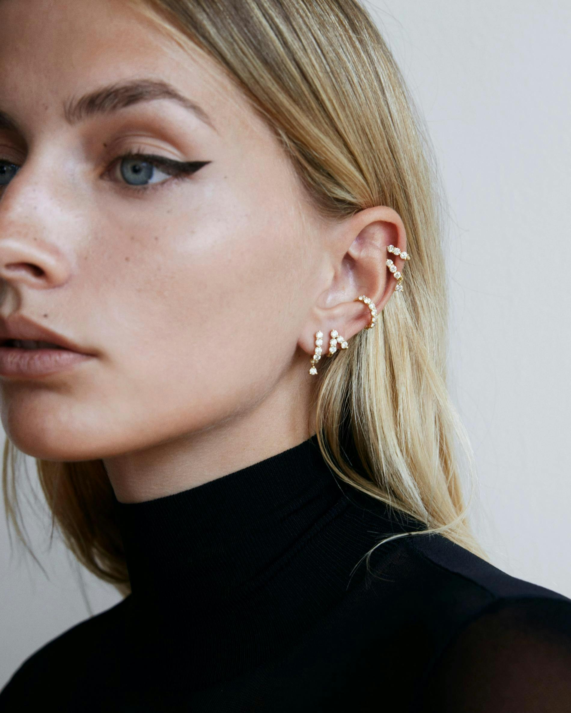 Model wearing multiple diamond earrings with black turtleneck